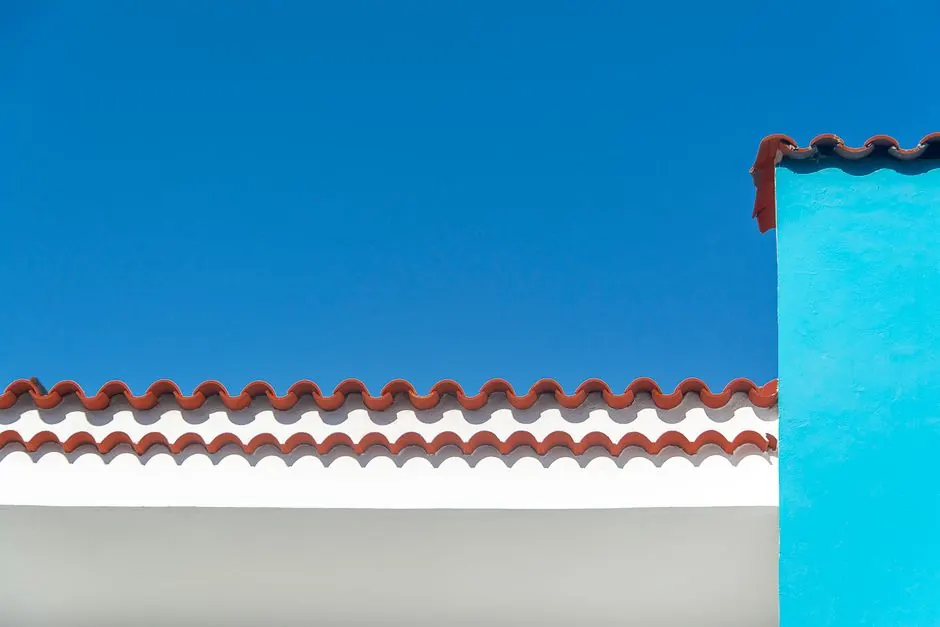 Red clay roof tiles on white building contrasting with clear blue sky, displaying minimalism.